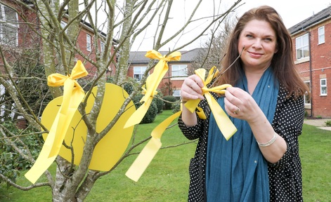 Artist Sarah Edwards at Welsh care home ties yellow ribbons around trees in memory of those who died of Covid. Credit: Pendine Park Care Organisation