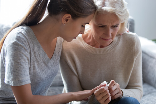 A young woman leaning in to comfort an upset, concerned older woman holding a tissue.